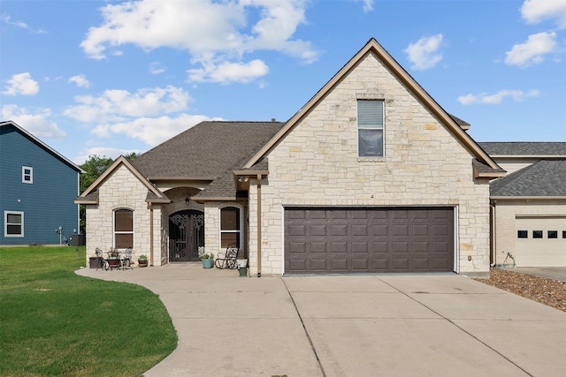 french country inspired facade featuring concrete driveway, a front lawn, and roof with shingles