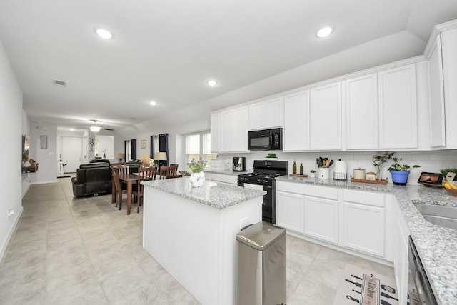 kitchen featuring black appliances, light stone counters, a center island, and white cabinets