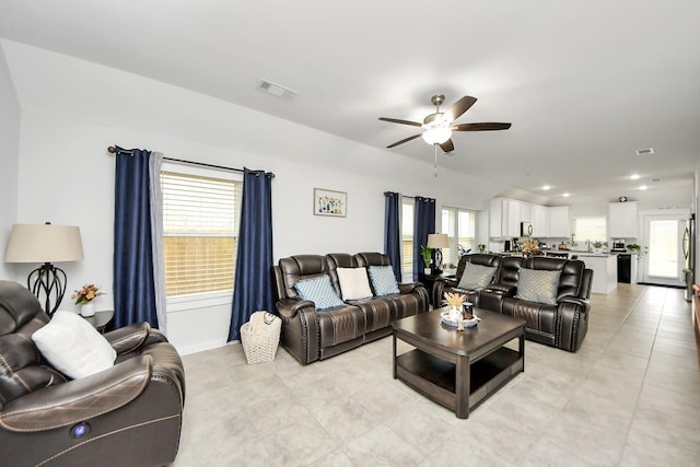 living area with a ceiling fan, a wealth of natural light, visible vents, and light tile patterned floors