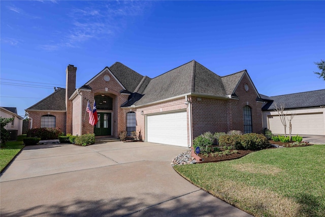 view of front of property with brick siding, a chimney, an attached garage, driveway, and a front lawn