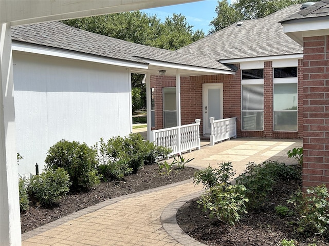 view of exterior entry with brick siding, covered porch, and roof with shingles