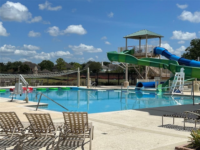 community pool with playground community, a patio area, fence, and a water slide