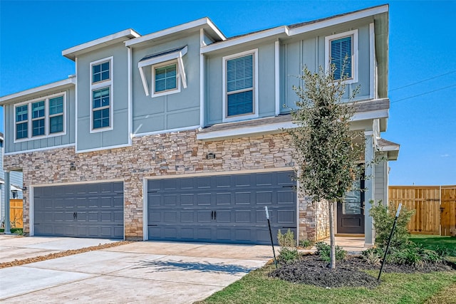 townhome / multi-family property featuring a garage, stone siding, board and batten siding, and fence