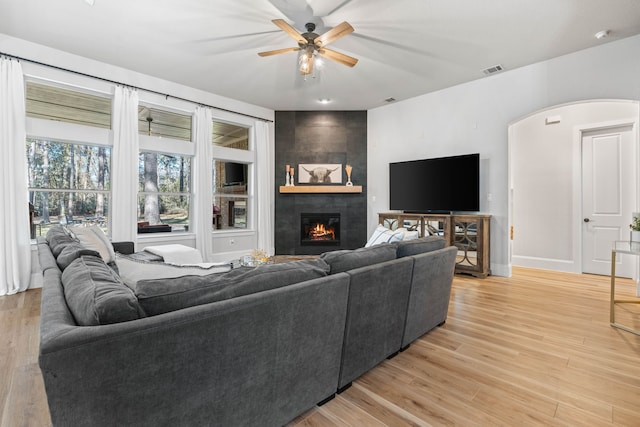 living area with arched walkways, visible vents, light wood-style flooring, a large fireplace, and ceiling fan