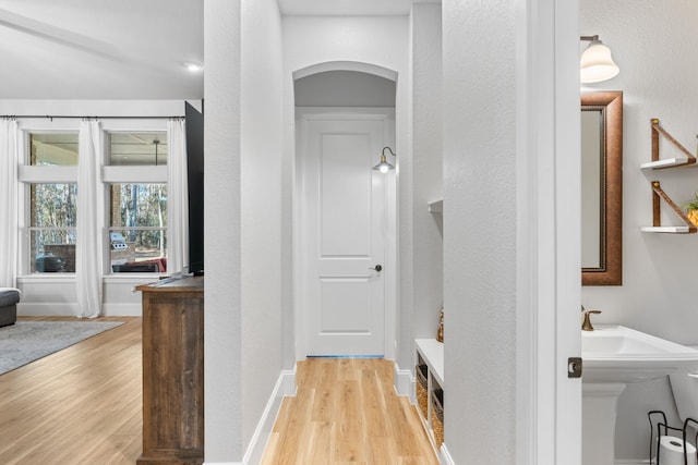 hall featuring arched walkways, light wood-style flooring, and baseboards