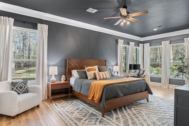 bedroom featuring light wood-type flooring, visible vents, a textured ceiling, and ornamental molding