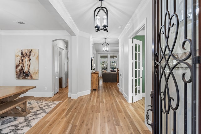 foyer entrance featuring a chandelier, arched walkways, light wood-style flooring, visible vents, and ornamental molding