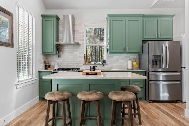 kitchen with a breakfast bar area, stainless steel fridge with ice dispenser, light wood-style flooring, green cabinets, and wall chimney exhaust hood