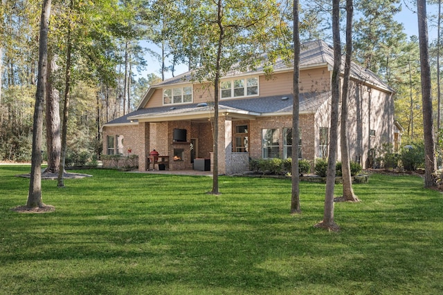 view of front of home with a front yard, a warm lit fireplace, brick siding, and a patio