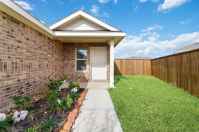 doorway to property with a yard, brick siding, and fence