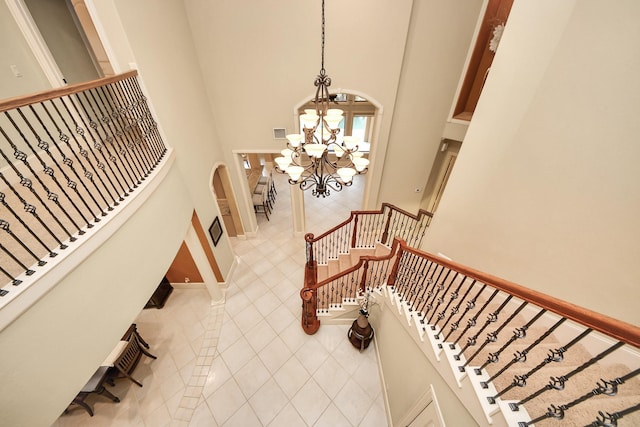 stairs with a towering ceiling, an inviting chandelier, tile patterned flooring, and baseboards