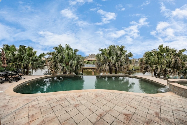 view of pool featuring a patio area, a water view, and a pool with connected hot tub