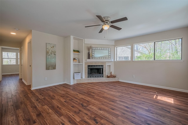 unfurnished living room with a tiled fireplace, dark wood-style floors, and baseboards