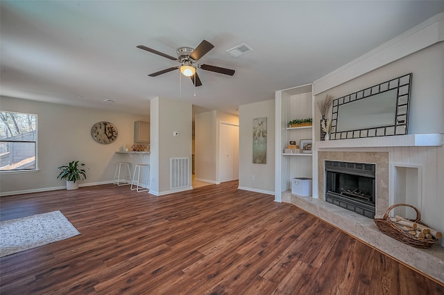 unfurnished living room with a tiled fireplace, visible vents, baseboards, and wood finished floors