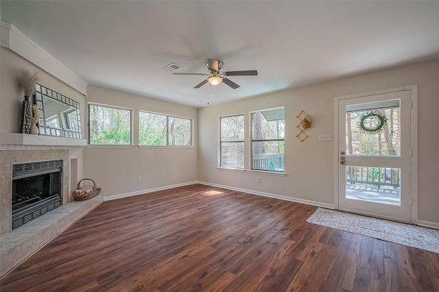 unfurnished living room with a tiled fireplace, visible vents, baseboards, and dark wood-style flooring