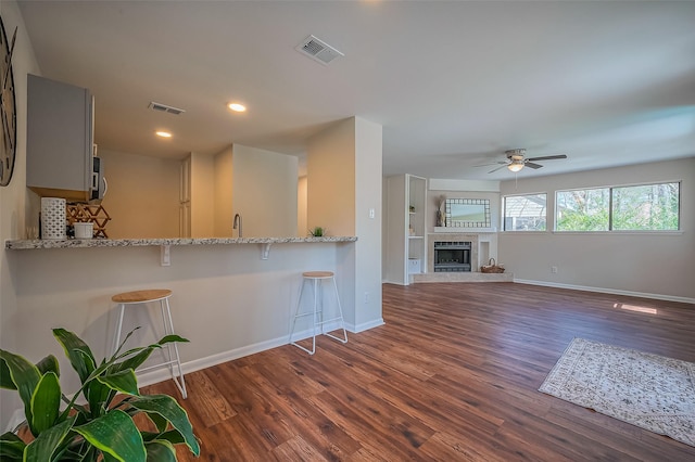 kitchen featuring a breakfast bar, dark wood-type flooring, visible vents, and a tiled fireplace