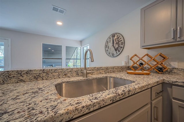 kitchen featuring visible vents, light stone countertops, gray cabinets, and a sink