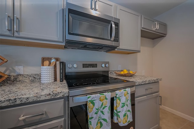 kitchen featuring light stone counters, stainless steel appliances, baseboards, and gray cabinets