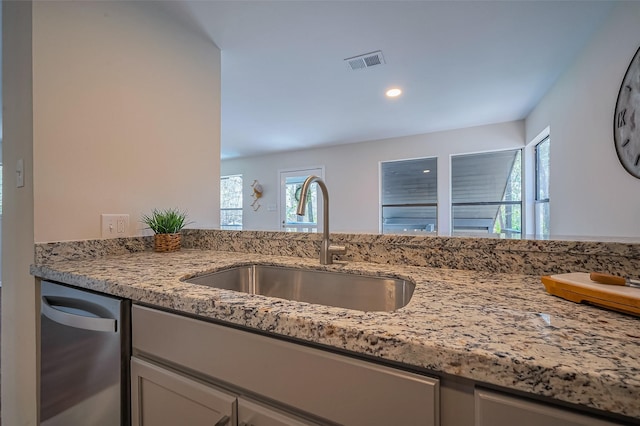 kitchen with stainless steel dishwasher, light stone countertops, visible vents, and a sink