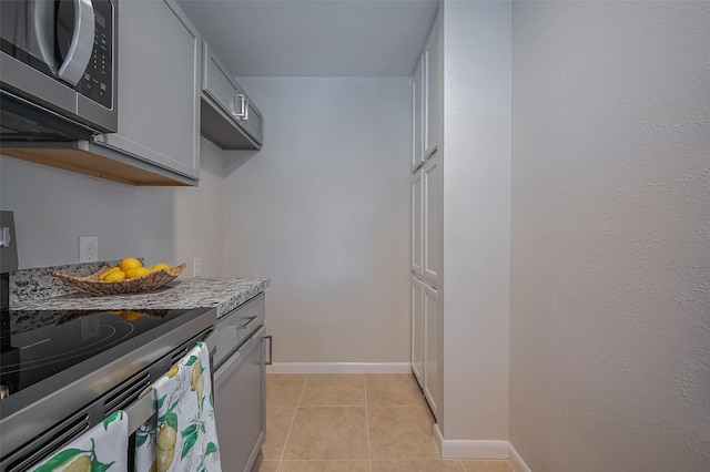 kitchen featuring light tile patterned flooring, stainless steel microwave, gray cabinetry, and baseboards