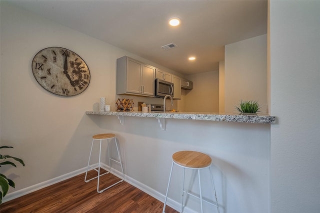 kitchen with a kitchen bar, visible vents, stainless steel microwave, baseboards, and dark wood-style flooring