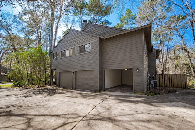 view of side of property with central AC unit, a chimney, concrete driveway, and an attached garage