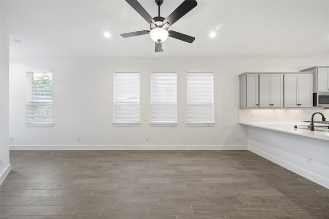 interior space featuring gray cabinetry, a ceiling fan, baseboards, light countertops, and stainless steel microwave