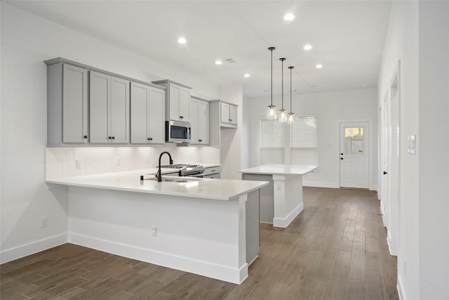 kitchen with a peninsula, a sink, light countertops, appliances with stainless steel finishes, and hanging light fixtures