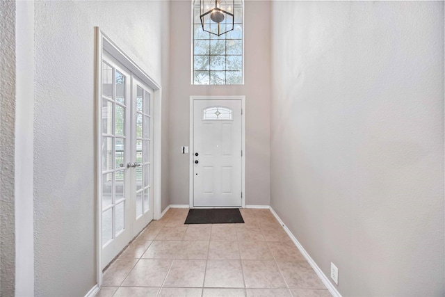 foyer entrance with light tile patterned floors, french doors, a high ceiling, and baseboards