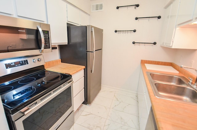 kitchen with stainless steel appliances, a sink, white cabinets, marble finish floor, and light countertops