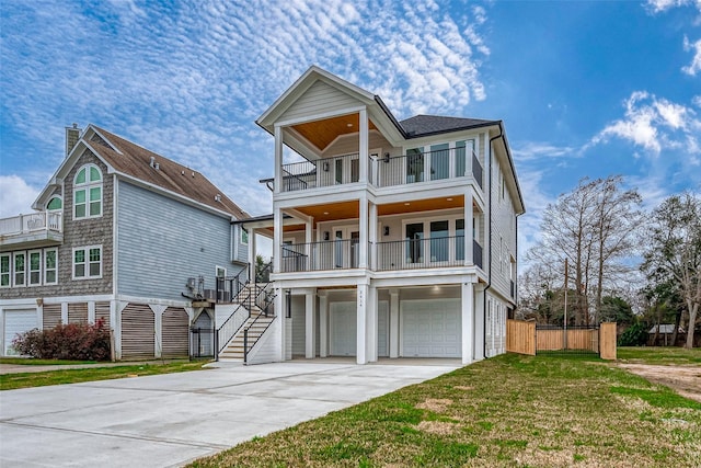 coastal inspired home with a garage, concrete driveway, a balcony, stairway, and a front lawn