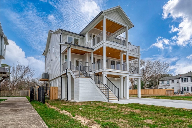 coastal home with a balcony, fence, stairs, concrete driveway, and a front yard