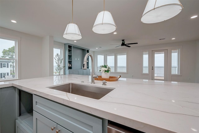 kitchen featuring recessed lighting, a sink, open floor plan, light stone countertops, and pendant lighting