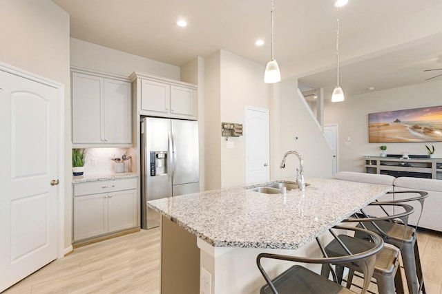 kitchen featuring stainless steel fridge, an island with sink, light stone countertops, pendant lighting, and a sink