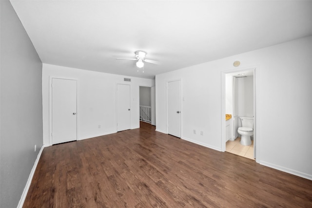 unfurnished bedroom with two closets, baseboards, visible vents, and dark wood-type flooring