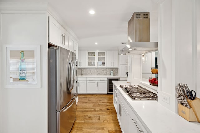 kitchen featuring beverage cooler, island range hood, appliances with stainless steel finishes, light countertops, and light wood-style floors