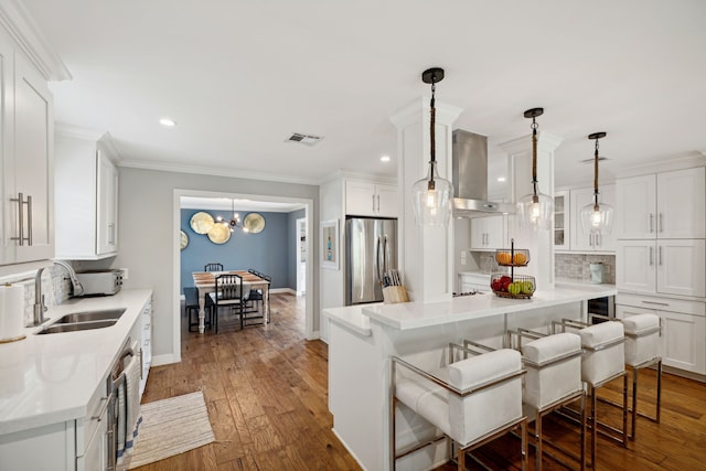 kitchen with a breakfast bar area, visible vents, white cabinets, stainless steel refrigerator, and island exhaust hood