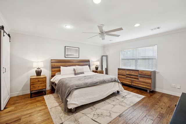 bedroom with light wood-style floors, a barn door, visible vents, and crown molding