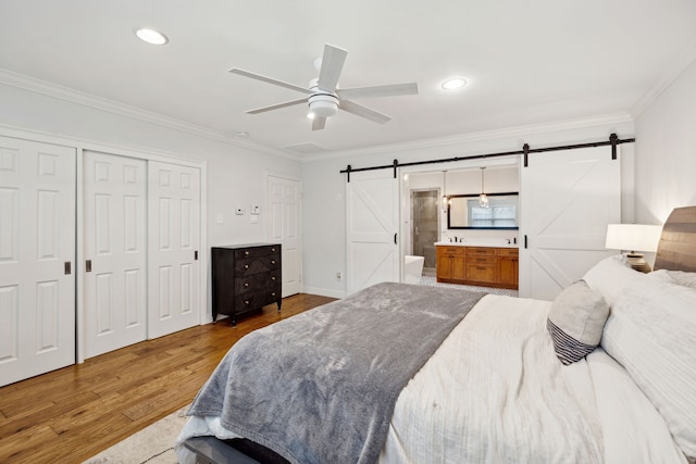 bedroom with a barn door, ceiling fan, wood finished floors, ensuite bathroom, and crown molding