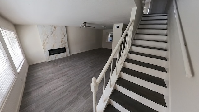 stairway with a ceiling fan, a fireplace, baseboards, and wood finished floors