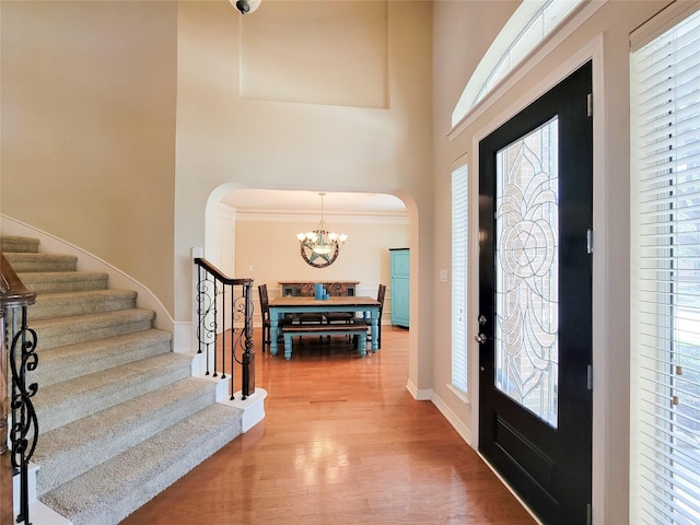 entryway with arched walkways, a notable chandelier, wood finished floors, baseboards, and stairs