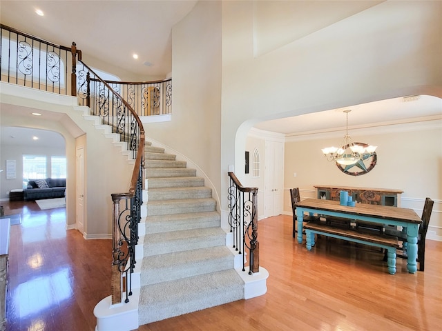 stairs featuring arched walkways, a notable chandelier, visible vents, a high ceiling, and wood finished floors