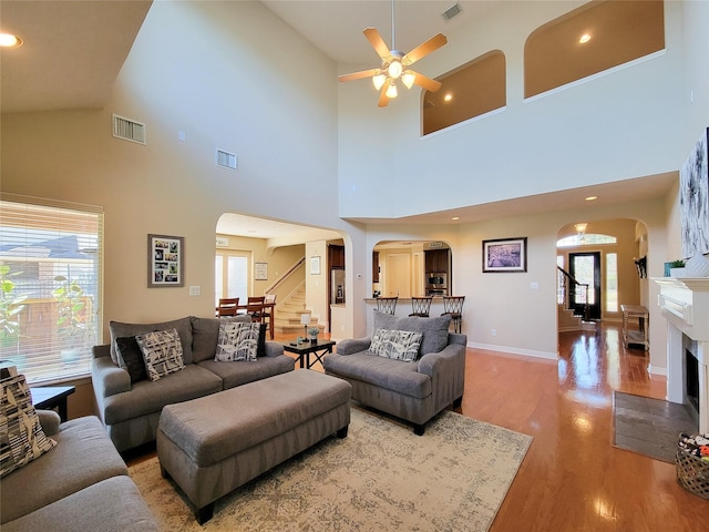 living room featuring a fireplace with flush hearth, arched walkways, visible vents, and wood finished floors