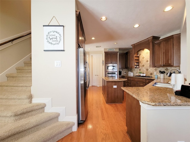 kitchen with stainless steel appliances, a sink, a center island, light wood-style floors, and light stone countertops