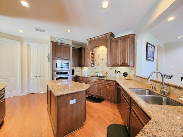 kitchen featuring light wood finished floors, stainless steel appliances, visible vents, a sink, and light stone countertops