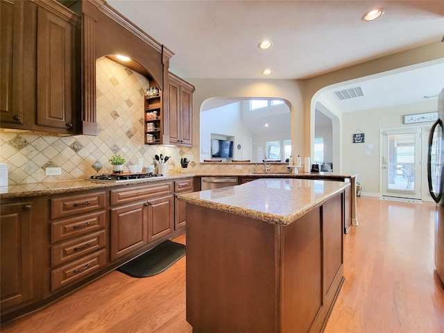 kitchen with light wood finished floors, visible vents, a kitchen island, appliances with stainless steel finishes, and vaulted ceiling