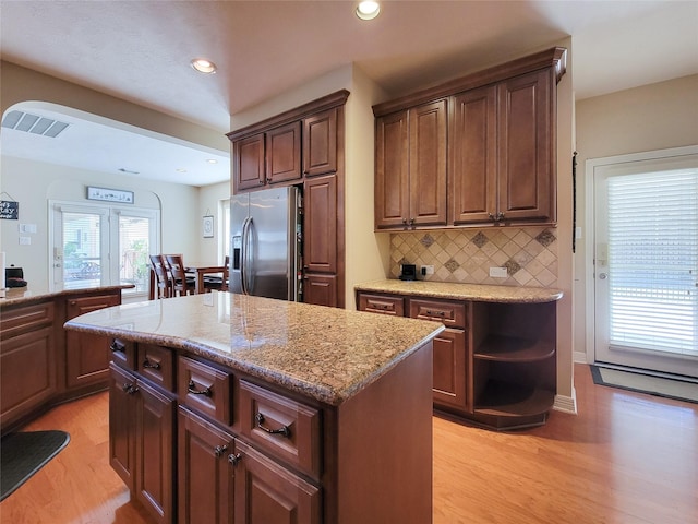 kitchen with a center island, tasteful backsplash, light wood-style flooring, dark brown cabinetry, and stainless steel fridge