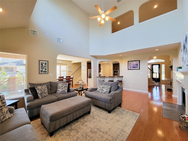 living room featuring arched walkways, wood finished floors, a fireplace with flush hearth, visible vents, and stairway