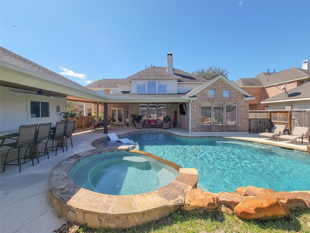 view of pool featuring ceiling fan, fence, a pool with connected hot tub, a bar, and a patio area