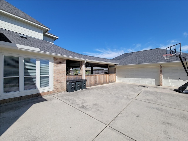 view of property exterior featuring a garage, roof with shingles, brick siding, and fence